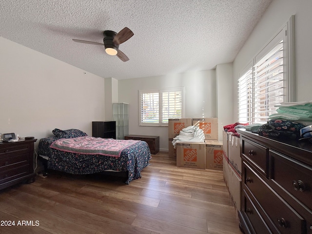 bedroom with hardwood / wood-style floors, ceiling fan, and a textured ceiling