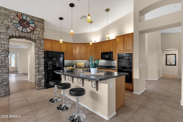 kitchen featuring a breakfast bar, backsplash, a high ceiling, black appliances, and an island with sink