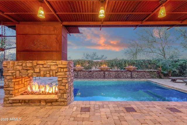 pool at dusk featuring an outdoor stone fireplace