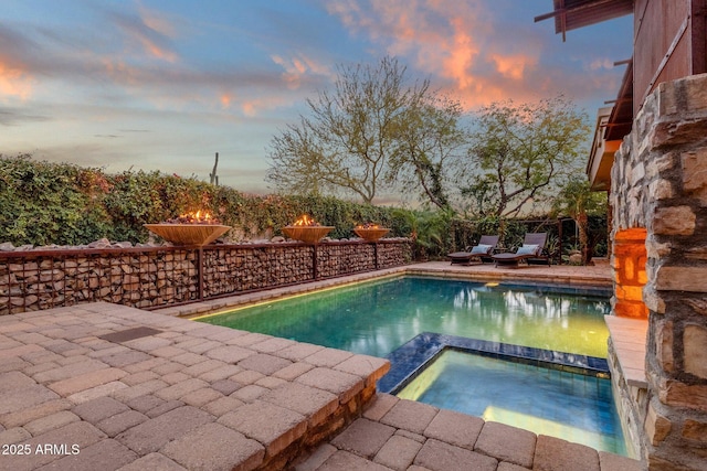 pool at dusk with a patio area and an in ground hot tub