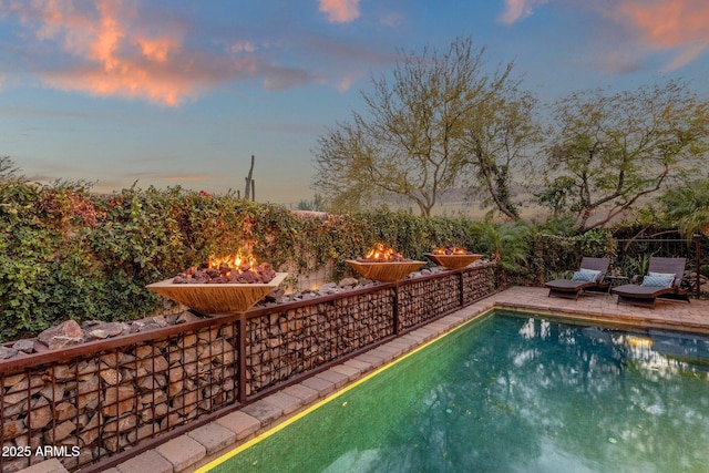 pool at dusk featuring an outdoor fire pit