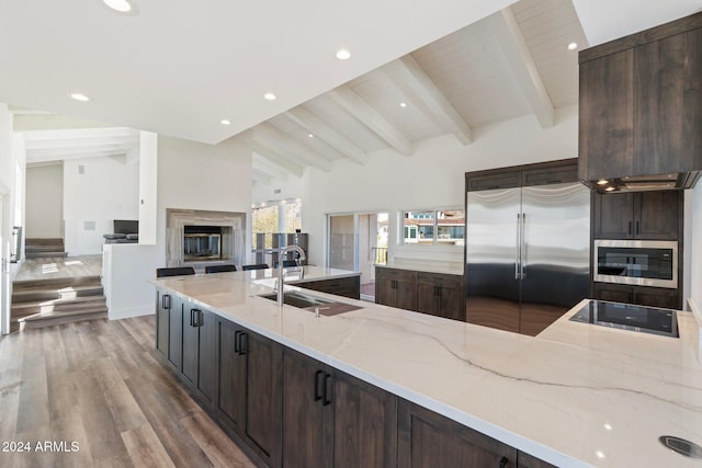 kitchen with beam ceiling, built in microwave, sink, light stone counters, and stainless steel fridge