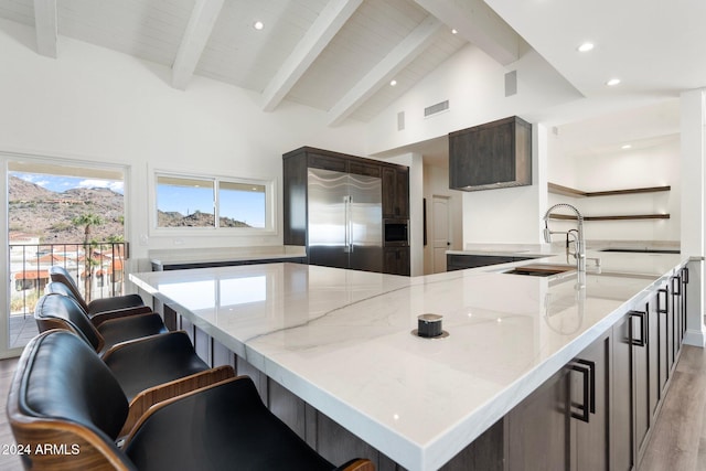 kitchen featuring appliances with stainless steel finishes, light wood-type flooring, light stone counters, and beam ceiling