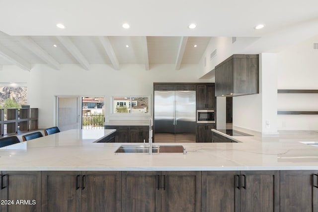 kitchen with light stone countertops, sink, beamed ceiling, a breakfast bar area, and appliances with stainless steel finishes