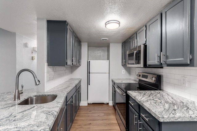 kitchen featuring sink, appliances with stainless steel finishes, gray cabinetry, light stone counters, and light hardwood / wood-style floors