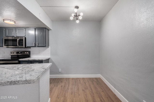 kitchen featuring gray cabinetry, a textured ceiling, appliances with stainless steel finishes, light hardwood / wood-style floors, and decorative backsplash