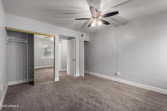 unfurnished bedroom featuring ceiling fan, a closet, a textured ceiling, and dark colored carpet