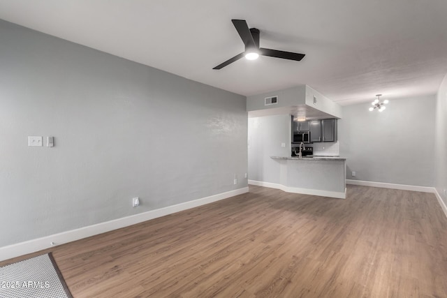 unfurnished living room featuring hardwood / wood-style floors, sink, and ceiling fan with notable chandelier