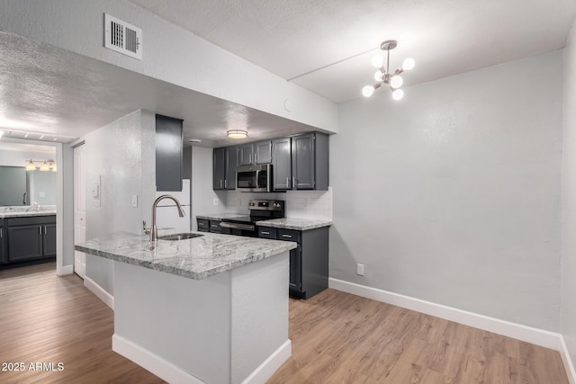 kitchen with sink, light stone counters, kitchen peninsula, stainless steel appliances, and light hardwood / wood-style flooring