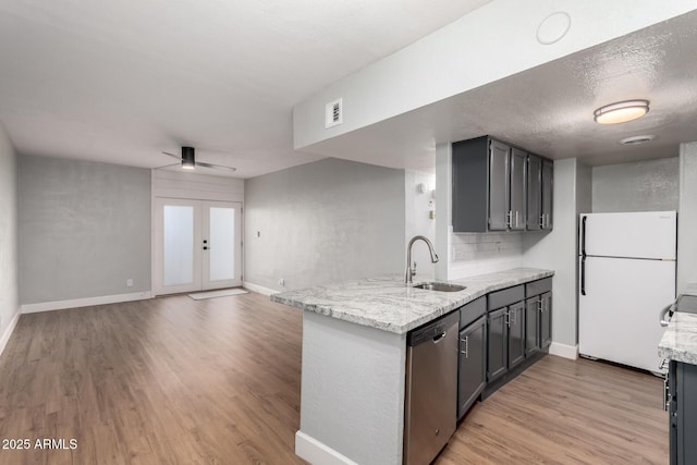 kitchen with sink, dishwasher, light stone counters, kitchen peninsula, and white fridge