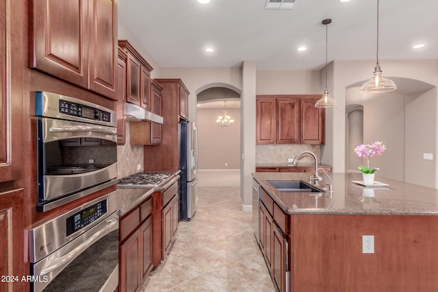 kitchen featuring stone counters, appliances with stainless steel finishes, a chandelier, sink, and a center island with sink