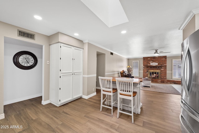 kitchen with freestanding refrigerator, a brick fireplace, visible vents, and wood finished floors