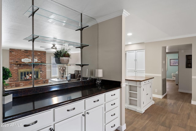 bar featuring crown molding, a ceiling fan, a fireplace, and wood finished floors