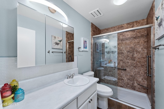 bathroom with a stall shower, visible vents, toilet, vanity, and backsplash