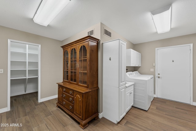 washroom with cabinet space, baseboards, visible vents, wood finished floors, and washing machine and clothes dryer