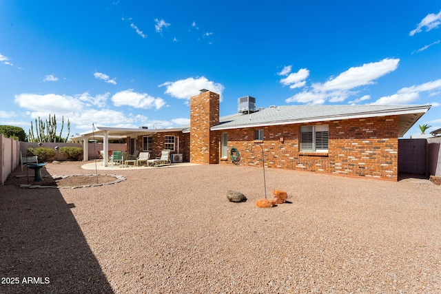 back of house featuring a fenced backyard, a chimney, a patio area, central AC, and brick siding