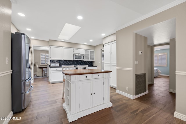 kitchen with butcher block counters, a skylight, visible vents, white cabinetry, and appliances with stainless steel finishes