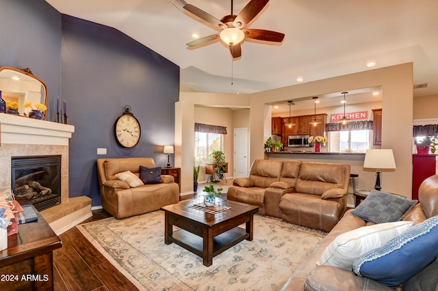 living room featuring ceiling fan, vaulted ceiling, a fireplace, and light hardwood / wood-style flooring