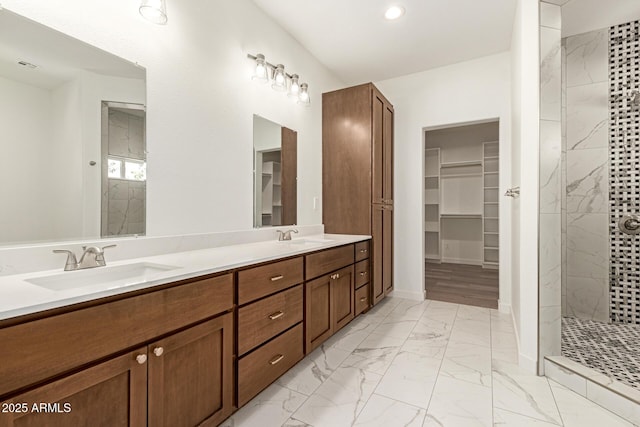 bathroom with double vanity, a walk in closet, a sink, marble finish floor, and tiled shower