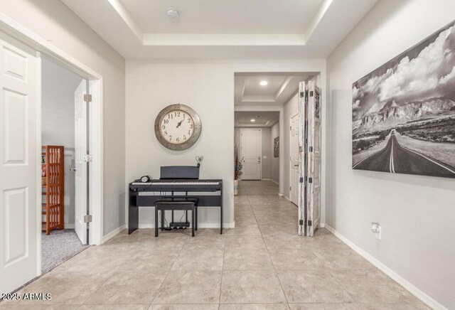 corridor featuring a tray ceiling, baseboards, and light tile patterned floors