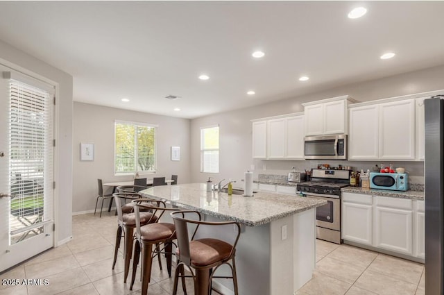 kitchen featuring recessed lighting, stainless steel appliances, light tile patterned floors, a center island with sink, and white cabinetry