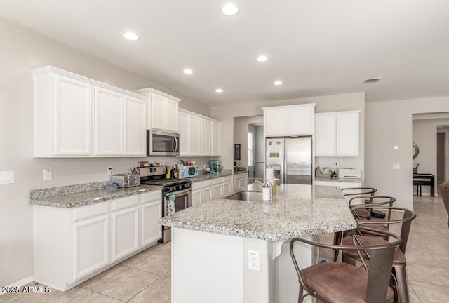 kitchen with a sink, an island with sink, a breakfast bar area, white cabinetry, and appliances with stainless steel finishes