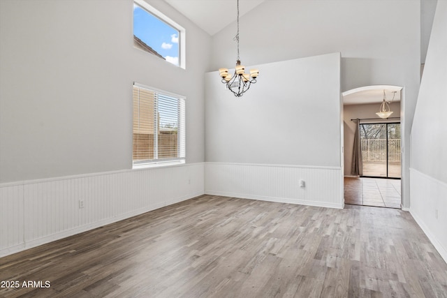 empty room featuring a wainscoted wall, arched walkways, a wealth of natural light, and an inviting chandelier