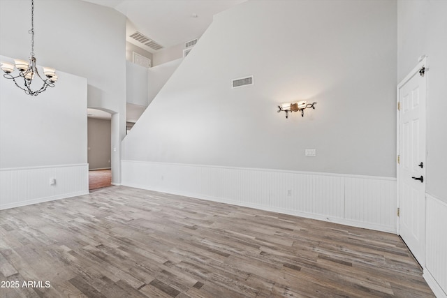 unfurnished room with wainscoting, wood finished floors, visible vents, and a notable chandelier