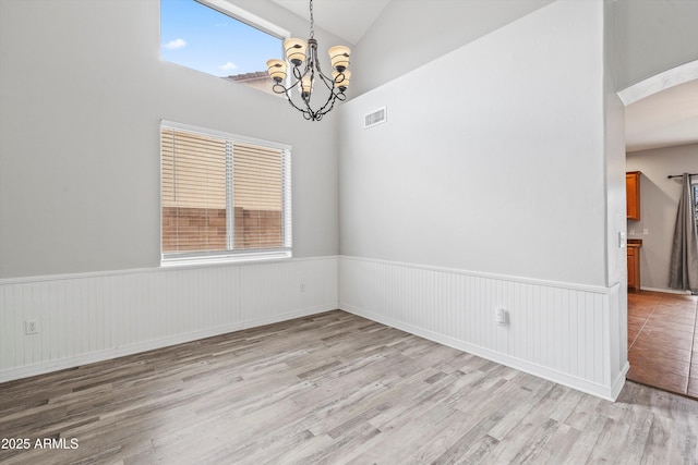 spare room with lofted ceiling, a chandelier, a wainscoted wall, visible vents, and light wood-style floors
