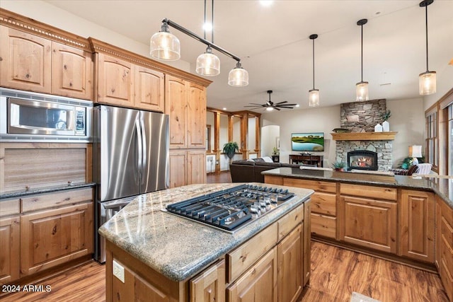 kitchen featuring stainless steel appliances, a stone fireplace, light wood-type flooring, a kitchen island, and ceiling fan