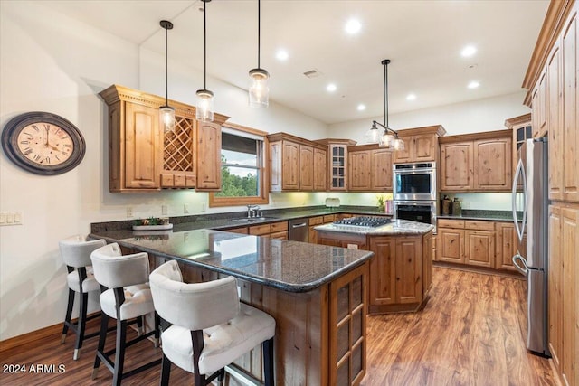 kitchen with stainless steel appliances, hanging light fixtures, a breakfast bar area, light wood-type flooring, and a center island