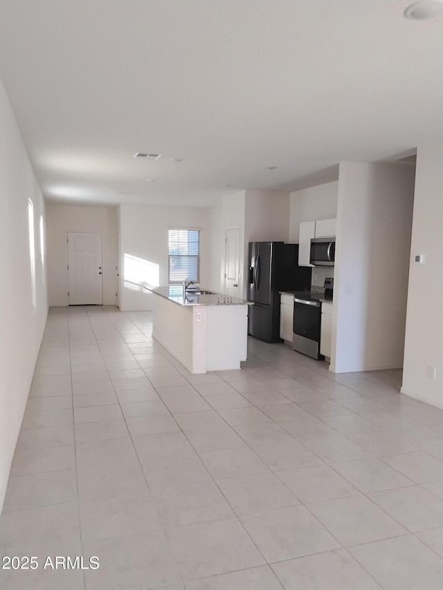 kitchen with light tile patterned floors, white cabinetry, stainless steel appliances, and a kitchen island with sink