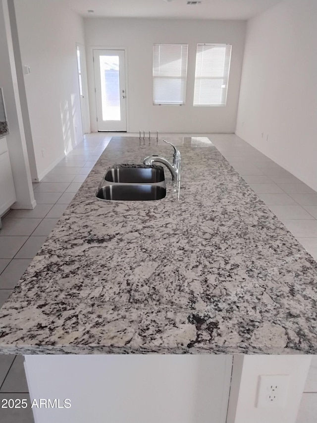 kitchen with white cabinets, light tile patterned floors, sink, and an island with sink