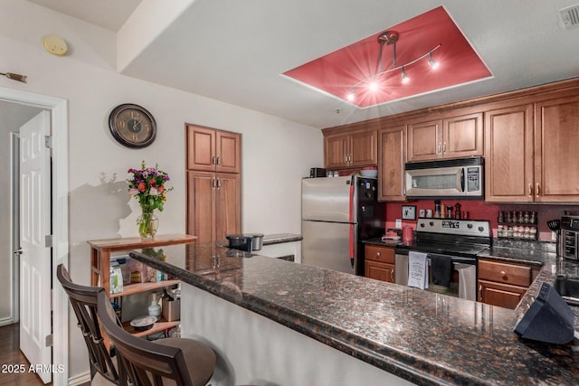 11375 E Sahuaro Dr Unit 1062, Scottsdale, AZ 85259 - kitchen featuring appliances with stainless steel finishes, brown cabinetry, dark stone counters, a kitchen bar, and a peninsula
