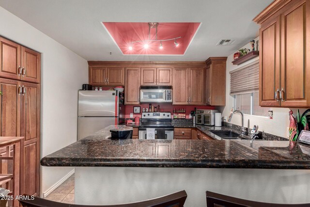 11375 E Sahuaro Dr Unit 1062, Scottsdale, AZ 85259 - kitchen featuring appliances with stainless steel finishes, a sink, brown cabinetry, a peninsula, and dark stone counters