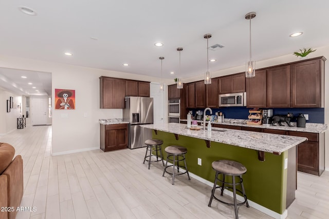 kitchen with a breakfast bar, sink, appliances with stainless steel finishes, an island with sink, and pendant lighting