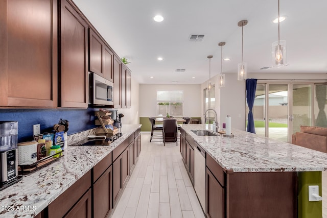 kitchen featuring appliances with stainless steel finishes, decorative light fixtures, sink, light stone counters, and light wood-type flooring