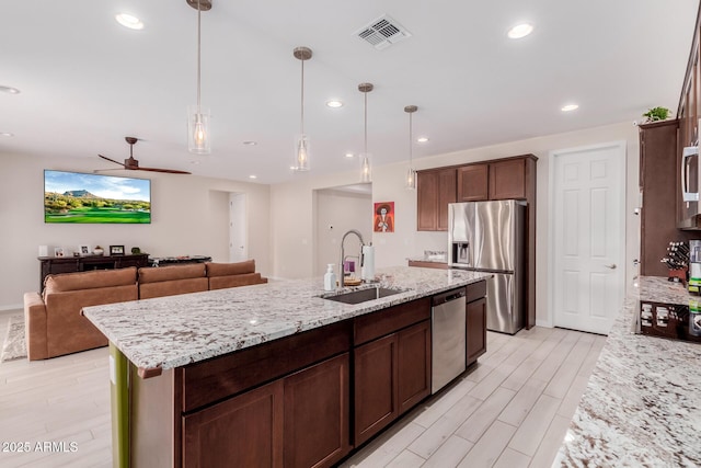 kitchen featuring sink, stainless steel appliances, hanging light fixtures, and a center island with sink