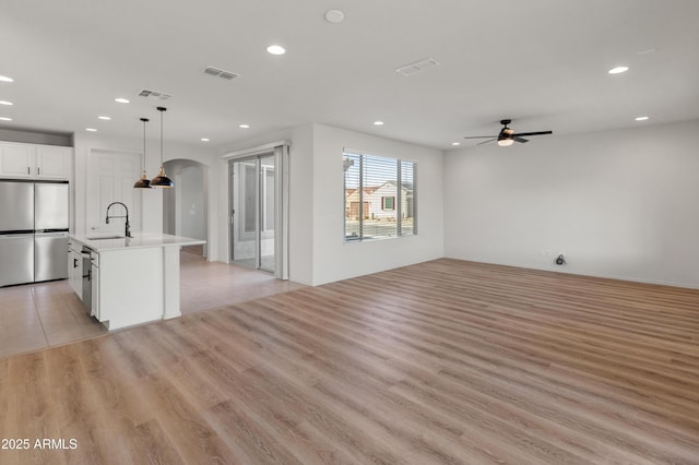 kitchen with white cabinetry, decorative light fixtures, light wood-type flooring, stainless steel fridge, and an island with sink