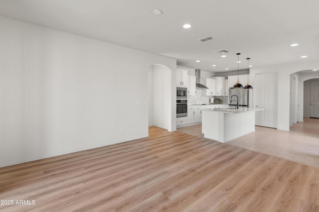 kitchen featuring light hardwood / wood-style flooring, a kitchen island with sink, stainless steel appliances, white cabinets, and decorative light fixtures