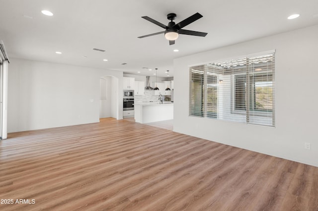 unfurnished living room with sink, ceiling fan, and light hardwood / wood-style flooring