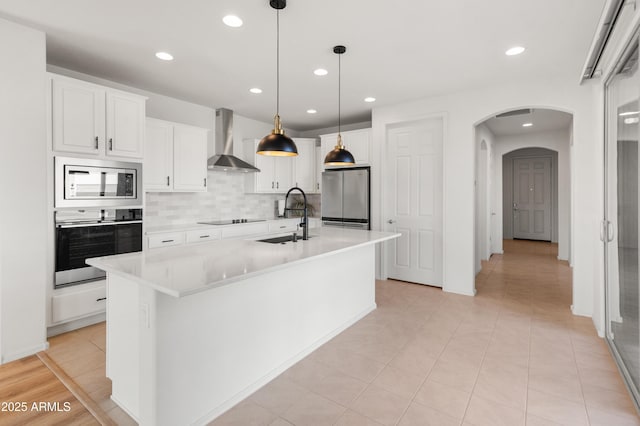 kitchen with stainless steel appliances, a center island with sink, sink, and wall chimney range hood