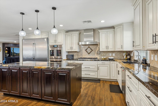 kitchen featuring pendant lighting, a kitchen island, wall chimney exhaust hood, stainless steel appliances, and dark hardwood / wood-style floors