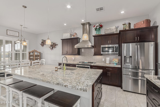 kitchen with a kitchen island with sink, stainless steel appliances, wall chimney range hood, and sink