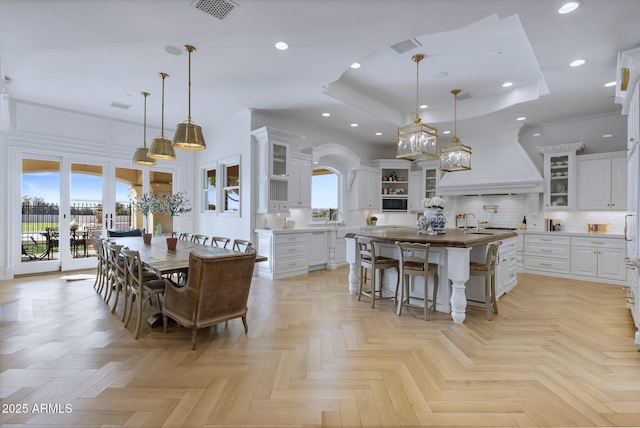 dining area featuring sink, a high ceiling, a raised ceiling, light parquet flooring, and french doors