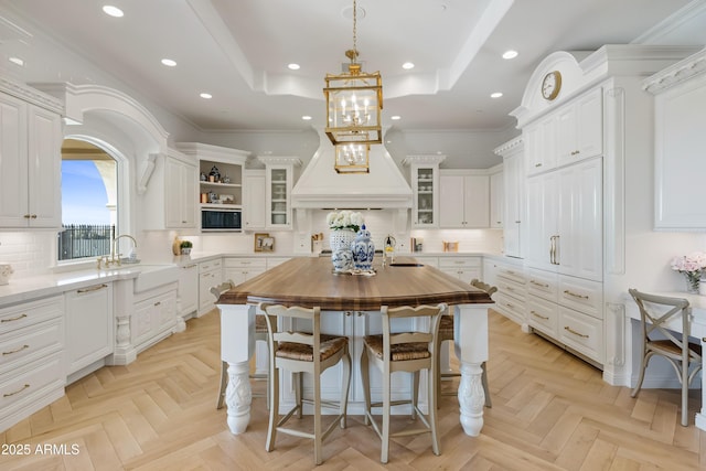 kitchen featuring butcher block countertops, white cabinetry, sink, light parquet floors, and a center island