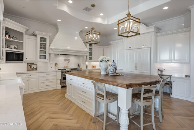 kitchen with custom exhaust hood, white cabinetry, black microwave, light parquet flooring, and high end stove