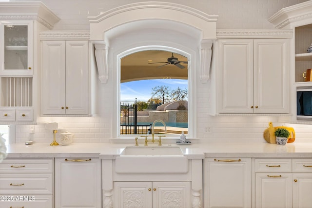 kitchen featuring tasteful backsplash, white cabinetry, sink, and ceiling fan