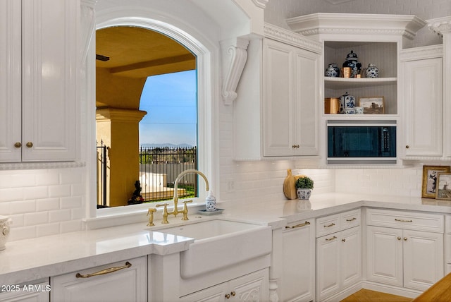 kitchen featuring light stone counters, sink, black microwave, and white cabinets