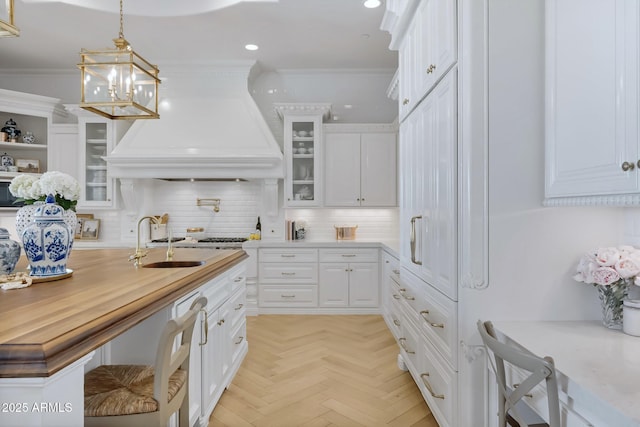 kitchen with premium range hood, crown molding, pendant lighting, light parquet floors, and white cabinets